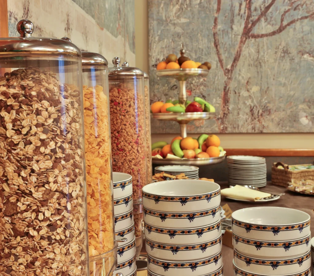 Primo piano di alcuni vasi contenenti cereali per la prima colazione e, sullo sfondo, della frutta fresca